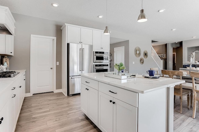 kitchen with a center island, white cabinets, light hardwood / wood-style floors, hanging light fixtures, and appliances with stainless steel finishes