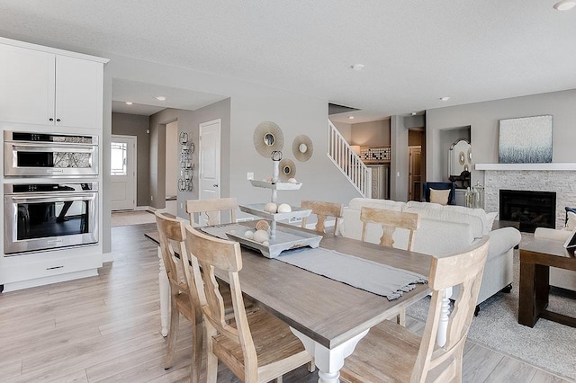 dining space with a stone fireplace, a textured ceiling, and light wood-type flooring