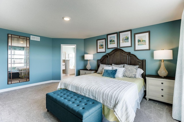 bedroom with ensuite bathroom, a textured ceiling, and light carpet