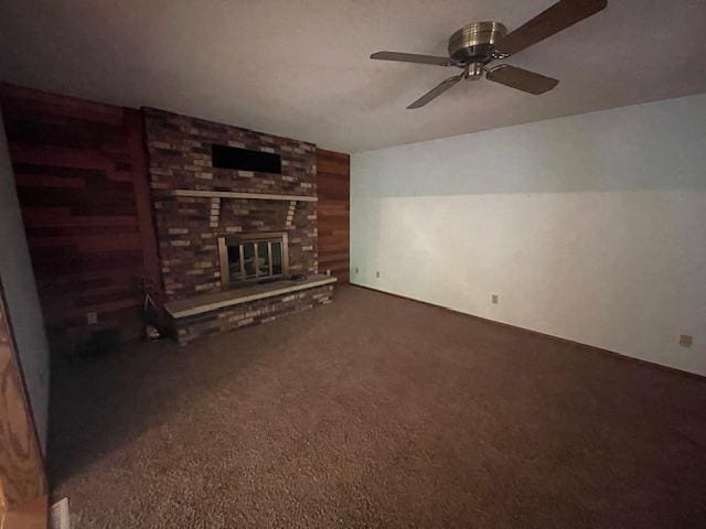 unfurnished living room featuring ceiling fan, wooden walls, a fireplace, and dark colored carpet