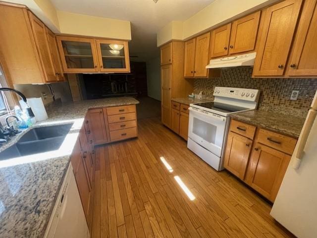 kitchen with tasteful backsplash, white appliances, light hardwood / wood-style flooring, dark stone countertops, and sink