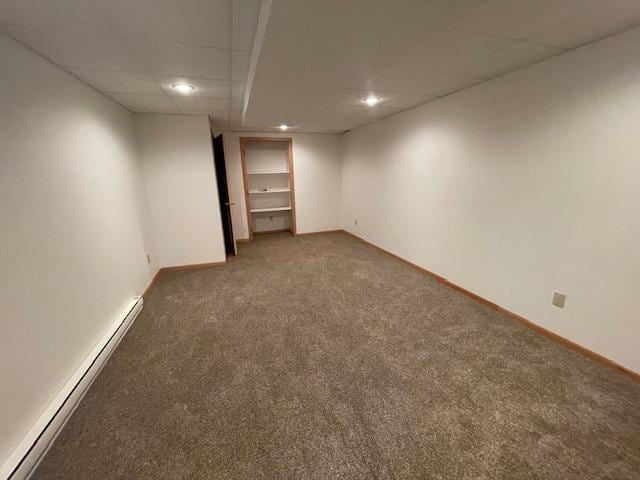 empty room with a drop ceiling, dark carpet, and baseboard heating