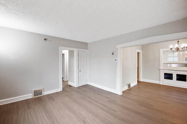 unfurnished living room featuring hardwood / wood-style floors, a textured ceiling, and an inviting chandelier