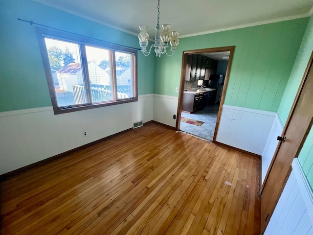 unfurnished dining area with light hardwood / wood-style floors, a notable chandelier, and crown molding