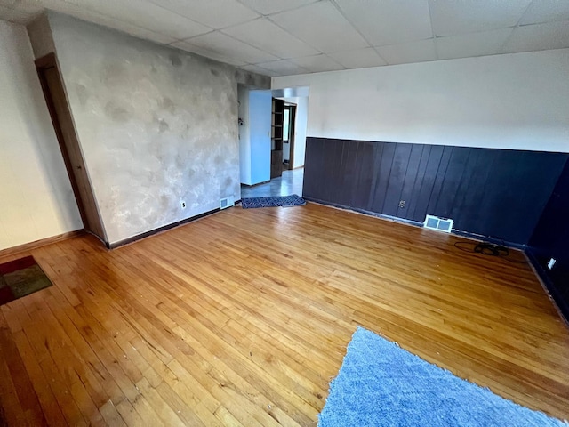 empty room featuring light hardwood / wood-style flooring, a paneled ceiling, and wood walls