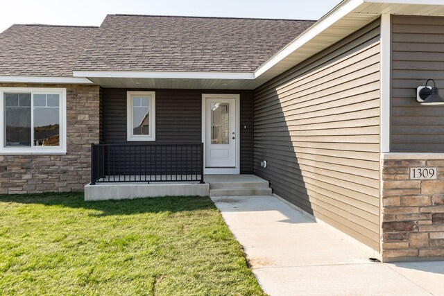 1309 18th St NE, Austin, MN 55912 - entrance to property with a yard, stone siding, a shingled roof, and covered porch