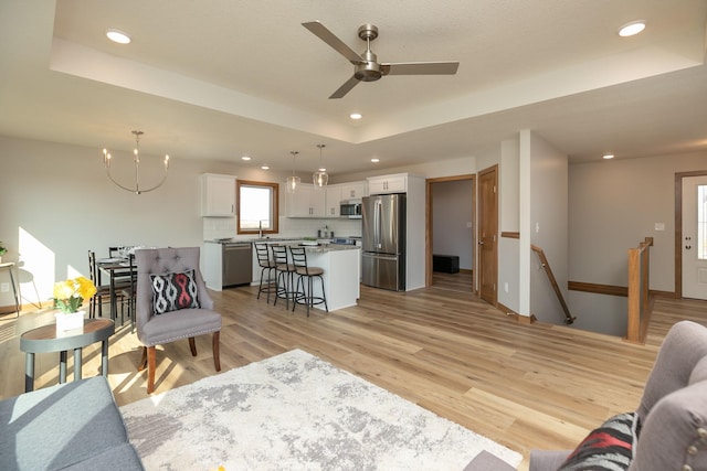 living room with ceiling fan, sink, a tray ceiling, and light hardwood / wood-style floors