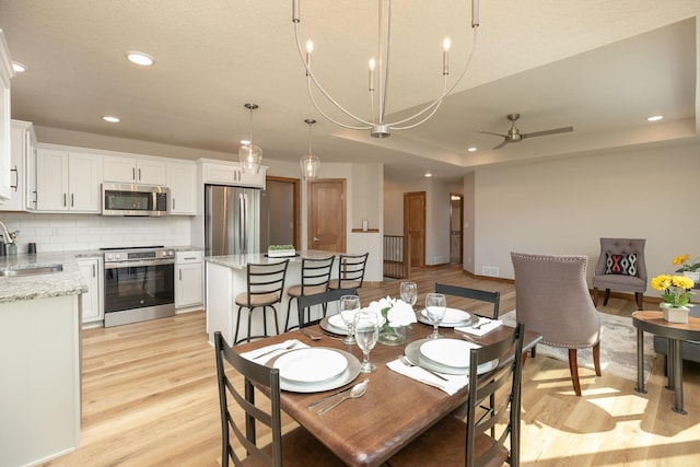 dining room featuring ceiling fan with notable chandelier, a textured ceiling, light hardwood / wood-style flooring, and sink