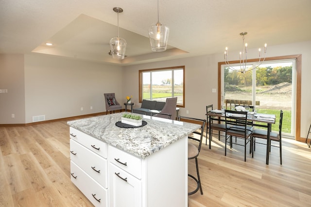 kitchen featuring light stone counters, decorative light fixtures, white cabinetry, a center island, and light wood-type flooring