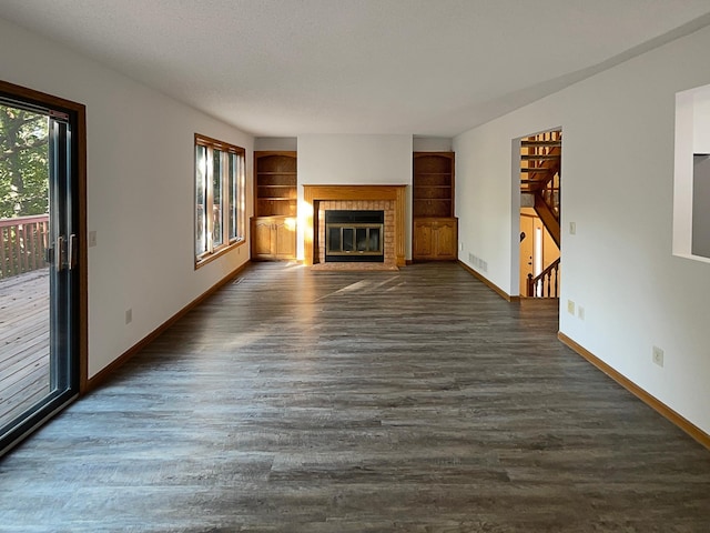 unfurnished living room with a brick fireplace, a textured ceiling, dark hardwood / wood-style floors, and built in features