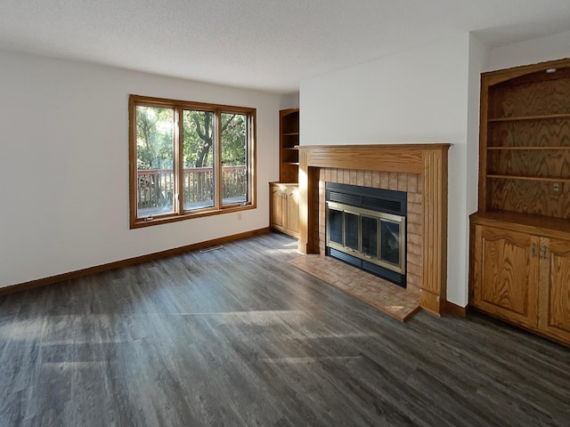 unfurnished living room with built in shelves, a tile fireplace, dark hardwood / wood-style floors, and a textured ceiling