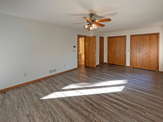 unfurnished bedroom with ceiling fan, multiple closets, and dark wood-type flooring