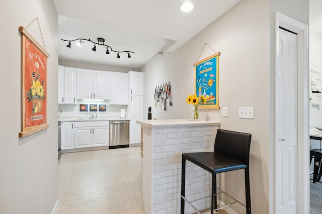 kitchen featuring kitchen peninsula, a breakfast bar, stainless steel dishwasher, and white cabinets