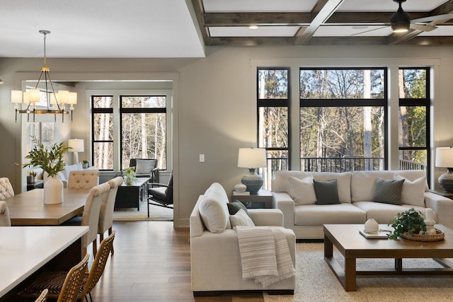 living room with coffered ceiling, ceiling fan with notable chandelier, wood-type flooring, and beamed ceiling