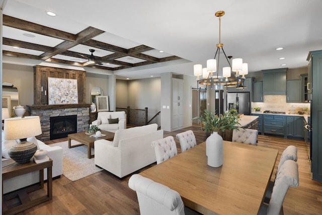 dining room with coffered ceiling, beam ceiling, dark wood-type flooring, and a stone fireplace