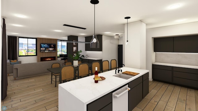 kitchen with dishwasher, sink, hanging light fixtures, light wood-type flooring, and an island with sink