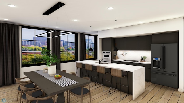 kitchen featuring pendant lighting, black appliances, a center island with sink, sink, and light hardwood / wood-style floors