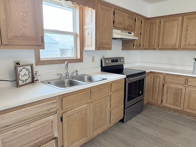 kitchen with a sink, light countertops, under cabinet range hood, and stainless steel range with electric cooktop