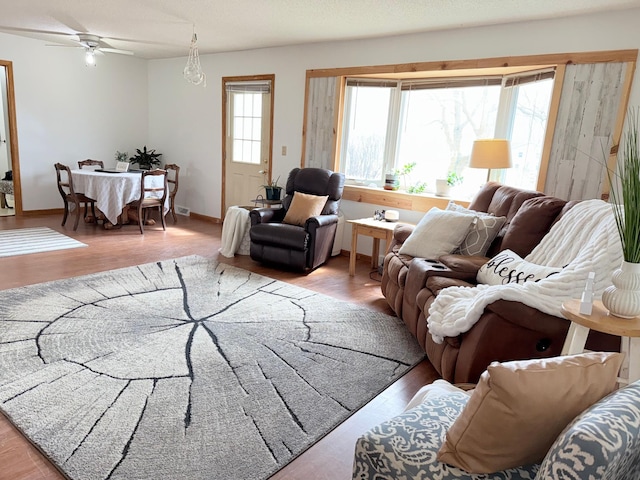 living area with baseboards, ceiling fan, and wood finished floors