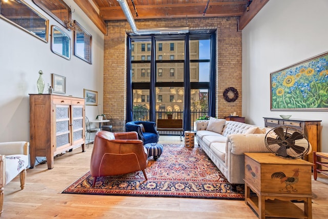 living room with beam ceiling, a towering ceiling, brick wall, wooden ceiling, and light wood-type flooring