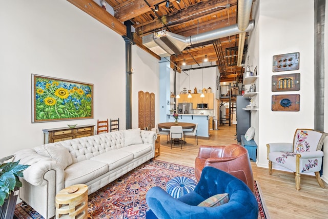 living room featuring beamed ceiling, a towering ceiling, light wood-type flooring, and wooden ceiling