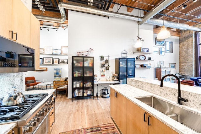 kitchen featuring pendant lighting, sink, cooktop, light wood-type flooring, and light stone counters