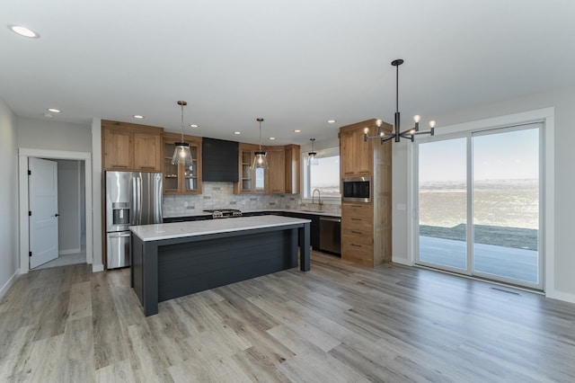 kitchen with pendant lighting, sink, appliances with stainless steel finishes, a center island, and light hardwood / wood-style floors