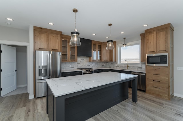 kitchen with sink, appliances with stainless steel finishes, hanging light fixtures, a center island, and light stone countertops