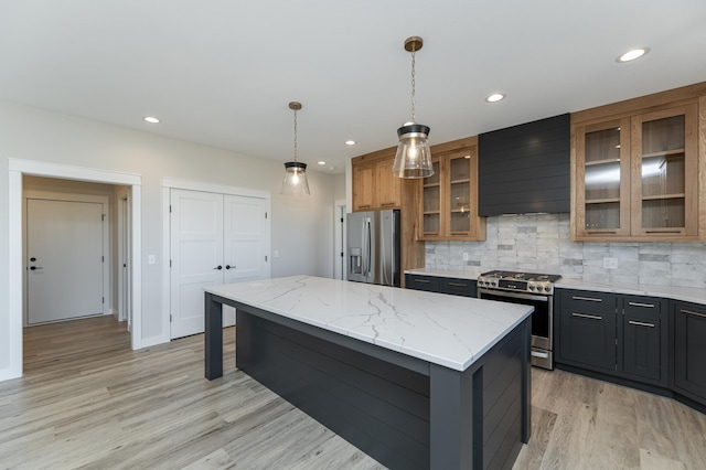 kitchen with a kitchen island, hanging light fixtures, stainless steel appliances, light stone countertops, and wall chimney exhaust hood