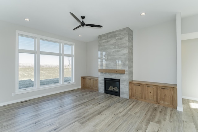 unfurnished living room featuring a tile fireplace, ceiling fan, and light wood-type flooring