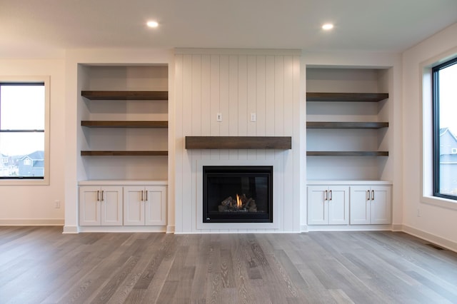 unfurnished living room featuring a wealth of natural light, a fireplace, light hardwood / wood-style flooring, and built in shelves