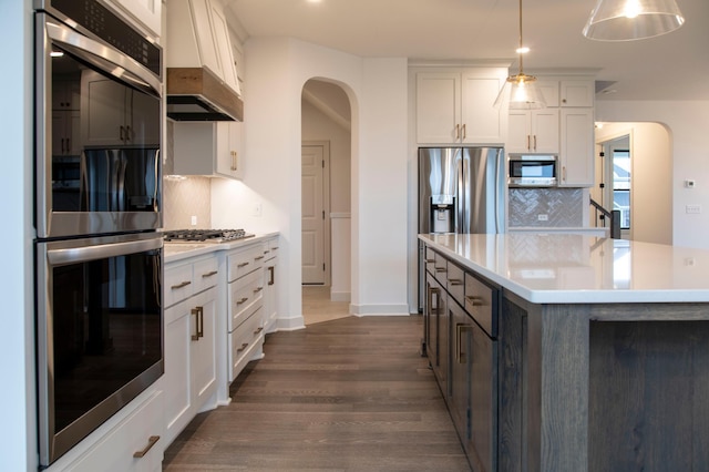 kitchen featuring white cabinets, backsplash, appliances with stainless steel finishes, and hanging light fixtures