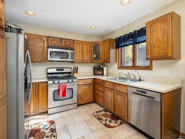 kitchen featuring a sink, appliances with stainless steel finishes, brown cabinetry, light countertops, and light tile patterned floors