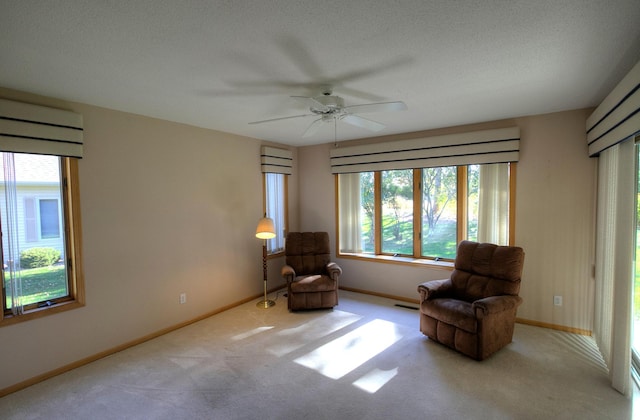 living area with ceiling fan, light colored carpet, and a textured ceiling