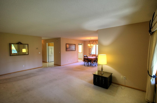 unfurnished living room featuring light colored carpet, a textured ceiling, baseboards, and a chandelier