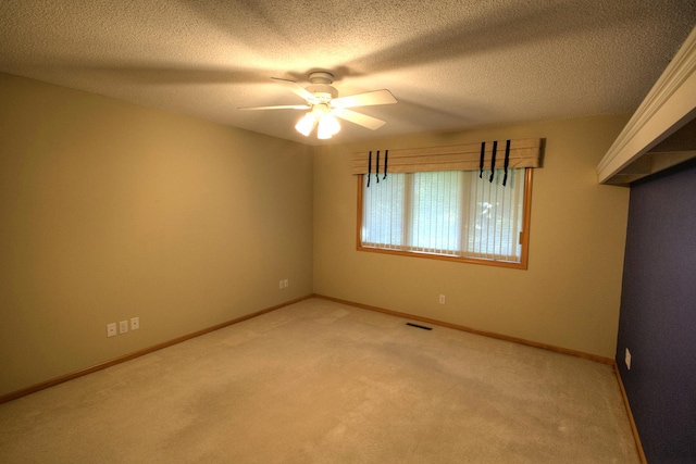 spare room featuring baseboards, a textured ceiling, visible vents, a ceiling fan, and light carpet