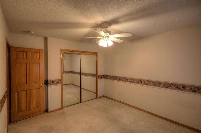 unfurnished bedroom with light colored carpet, baseboards, a textured ceiling, ceiling fan, and a closet