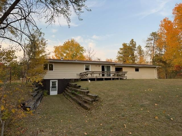 back house at dusk with a wooden deck and a lawn