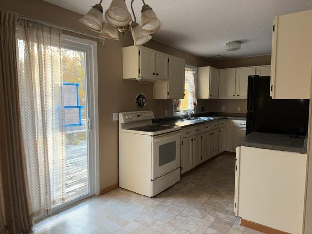 kitchen featuring a chandelier, electric range, black fridge, sink, and white cabinets