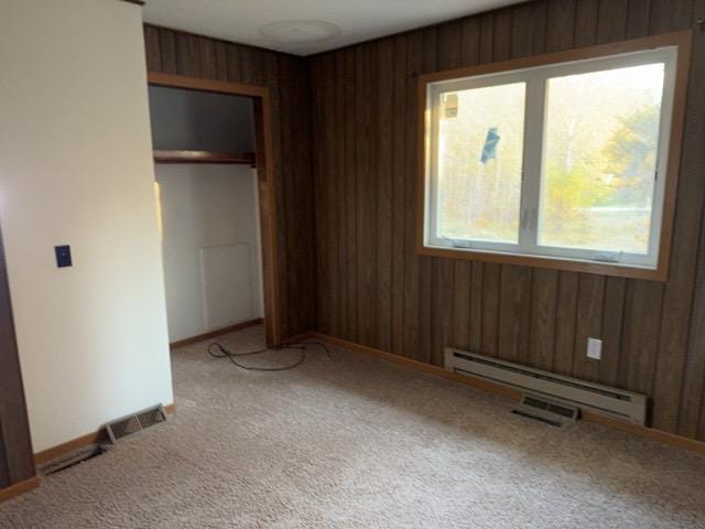 unfurnished bedroom with carpet flooring, a baseboard heating unit, and wooden walls