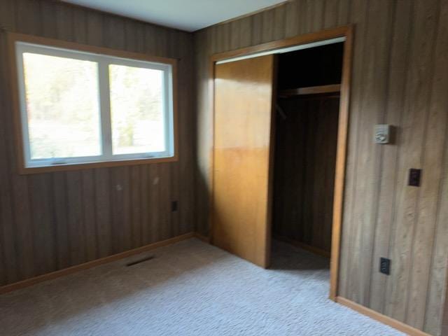 unfurnished bedroom with light carpet, wooden walls, a closet, and multiple windows