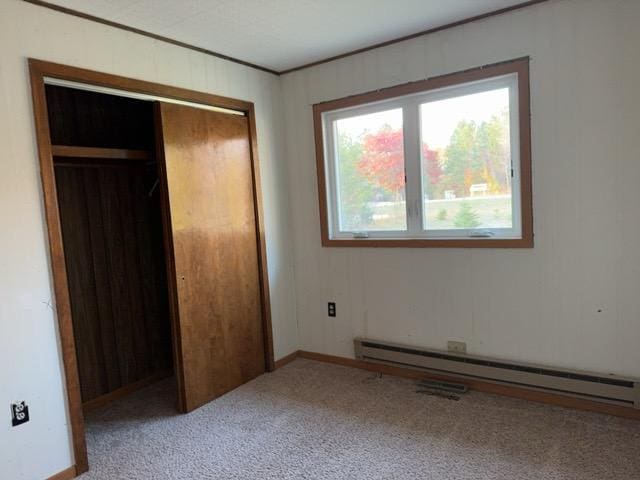 unfurnished bedroom featuring light colored carpet, a closet, and baseboard heating