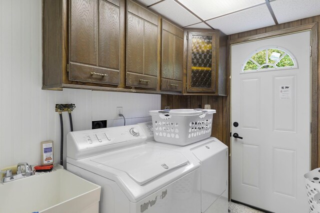 laundry room with wooden walls, cabinets, sink, and washing machine and dryer