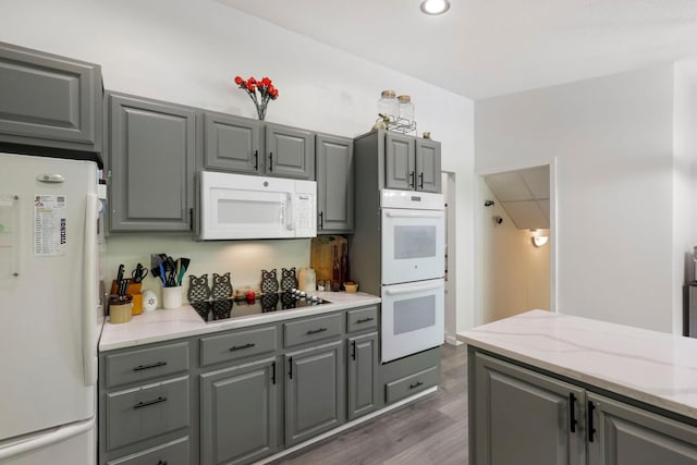 kitchen with gray cabinetry, light stone countertops, dark hardwood / wood-style floors, and white appliances