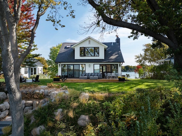 rear view of house featuring a deck with water view, an outdoor hangout area, a lawn, and a chimney