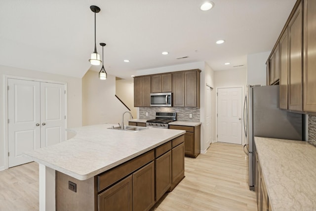 kitchen featuring sink, a center island with sink, appliances with stainless steel finishes, pendant lighting, and decorative backsplash