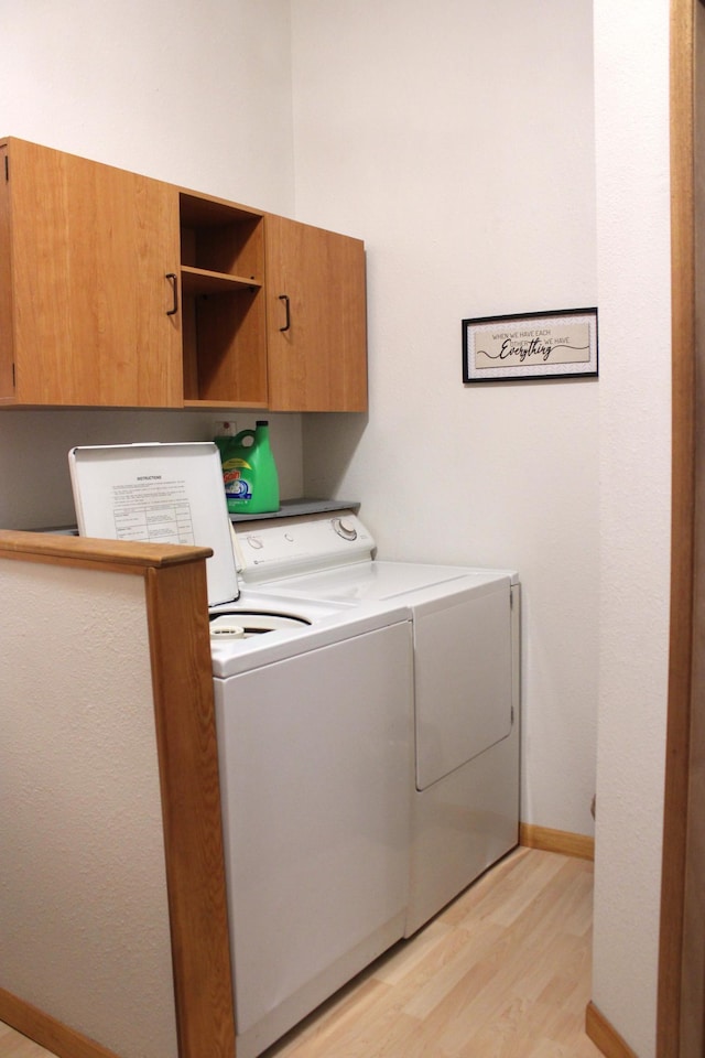 clothes washing area featuring washing machine and dryer, light hardwood / wood-style floors, and cabinets