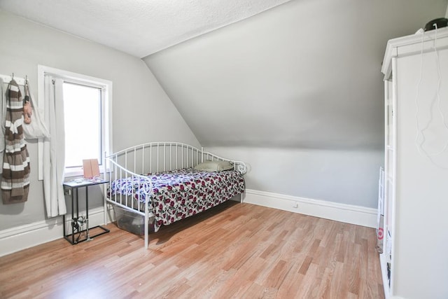 bedroom with lofted ceiling, light wood-type flooring, and a textured ceiling