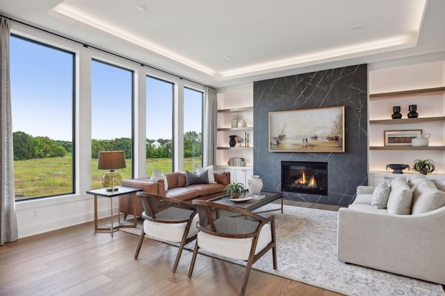 living room with a high end fireplace, wood-type flooring, built in features, and a raised ceiling