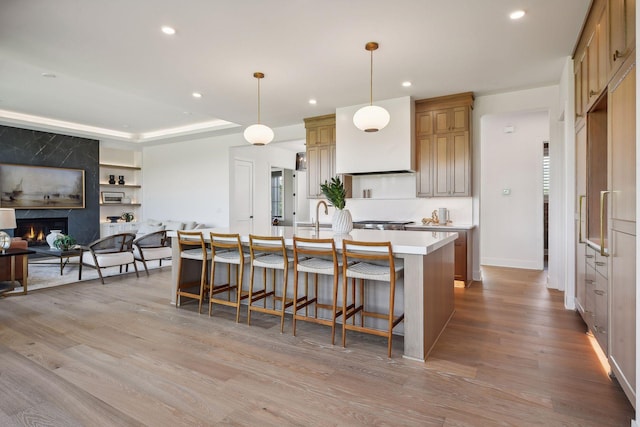 kitchen featuring a kitchen bar, a high end fireplace, pendant lighting, light hardwood / wood-style flooring, and a kitchen island with sink